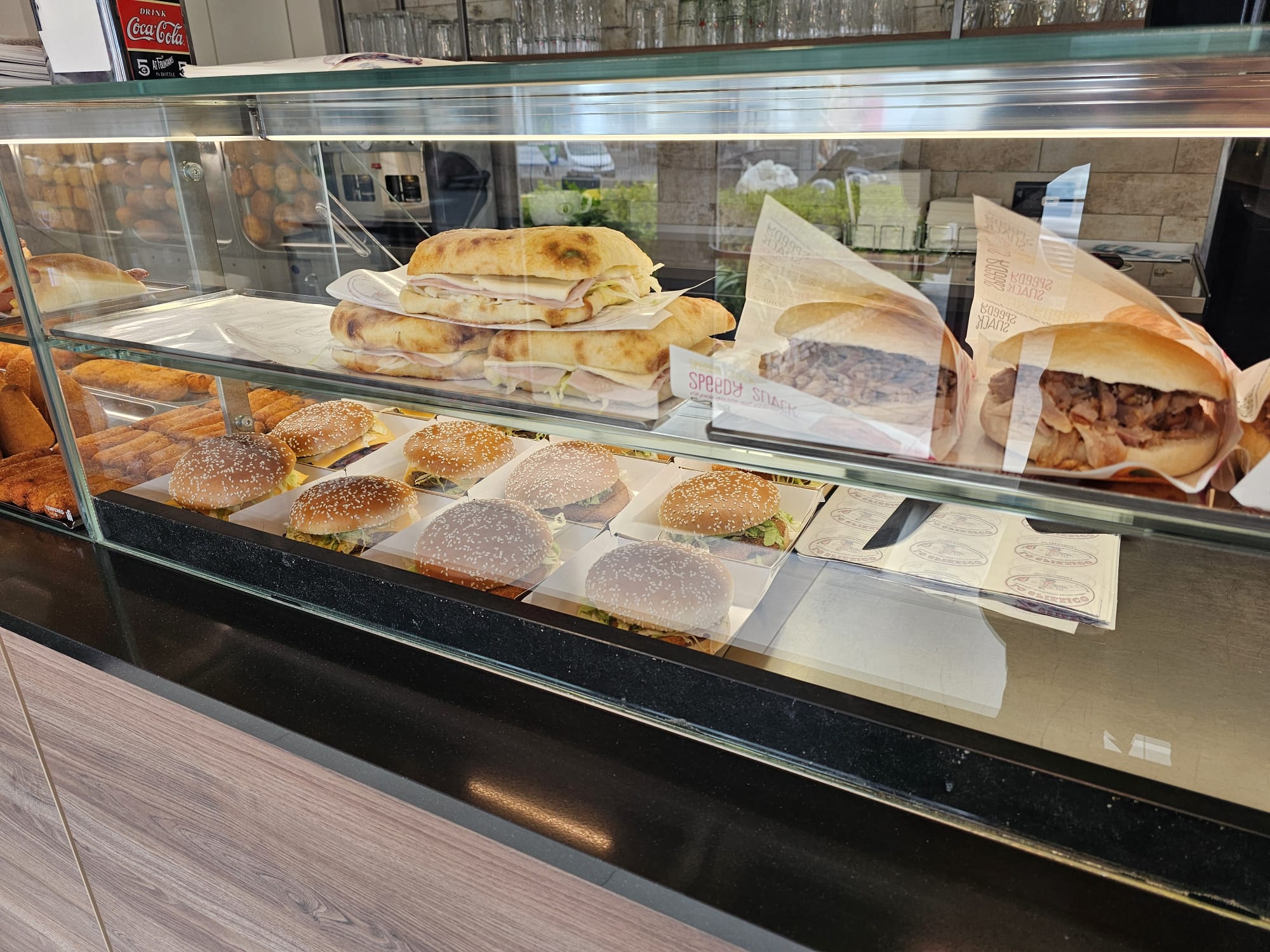 Vetrina di Lo Spizzico con burger al sesamo, pizze farcite al prosciutto e panini con carne in carta Speedy Snack