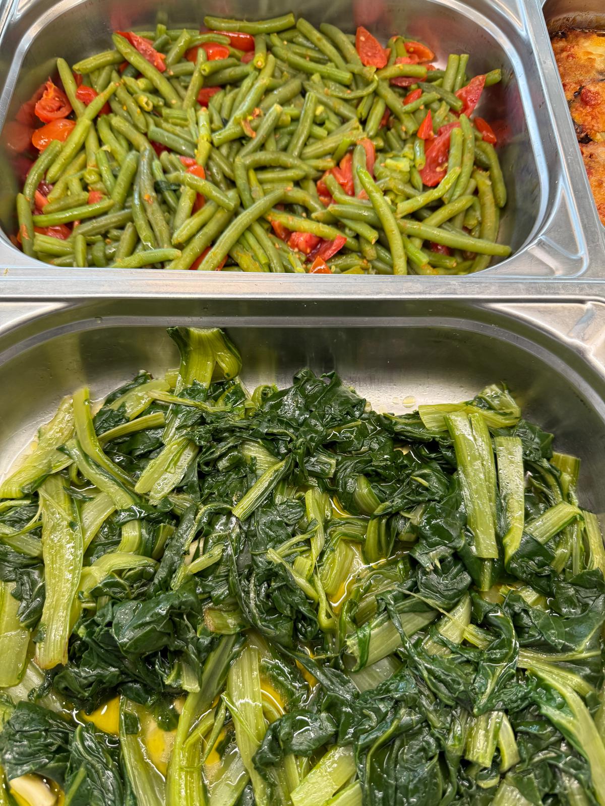 Fagiolini con pomodorini e bietole lessate all'olio in vaschette d'acciaio sul banco di Lo Spizzico