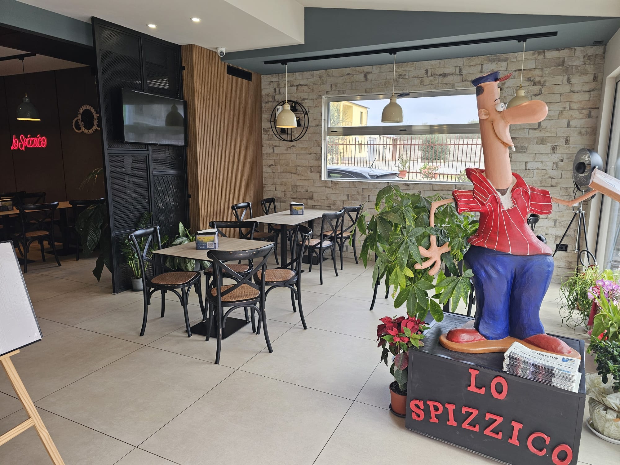 Sala di Lo Spizzico con tavoli in legno, sedie nere, muro in pietra e statua di pizzaiolo su base con la scritta LO SPIZZICO
